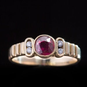 Op de afbeelding: Een gouden ring met een rode robijn en kleine diamanten op de band.