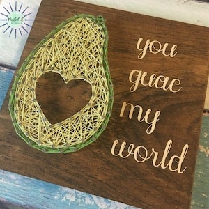 May include: String art of an avocado with a heart in the middle. The text "You guac my world" is written on the wooden background.