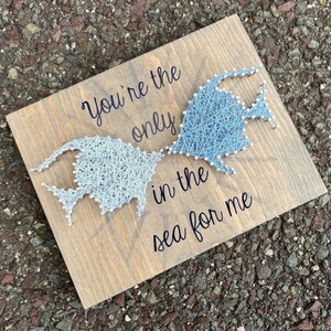 May include: A wooden sign with a blue and white string art design of two fish facing each other. The sign reads "You're the only in the sea for me."