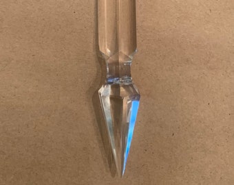 Puede incluir: Un colgante de cristal de prisma de araña transparente con una parte superior octogonal facetada y una parte inferior puntiaguda.