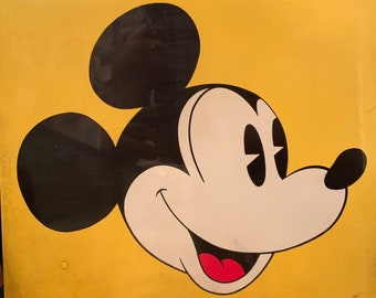 May include: A yellow square metal sign with a black and white image of Mickey Mouse's head. Mickey Mouse is smiling with his tongue sticking out. The sign has the copyright information "© Walt Disney Productions" in the bottom right corner.