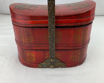 Puede incluir: Una caja de madera roja de dos niveles con un asa de latón y detalles decorativos. La caja está decorada con caracteres chinos dorados y un diseño de dragón.
