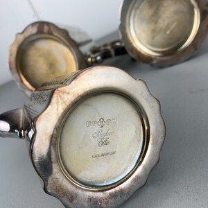 Puede incluir: Primer plano de piezas de juego de t&eacute; de plata antiguas. Las piezas tienen un dise&ntilde;o de borde festoneado y est&aacute;n estampadas con "Barker Ellis" y "Made in England". La plata tiene un aspecto deslustrado.