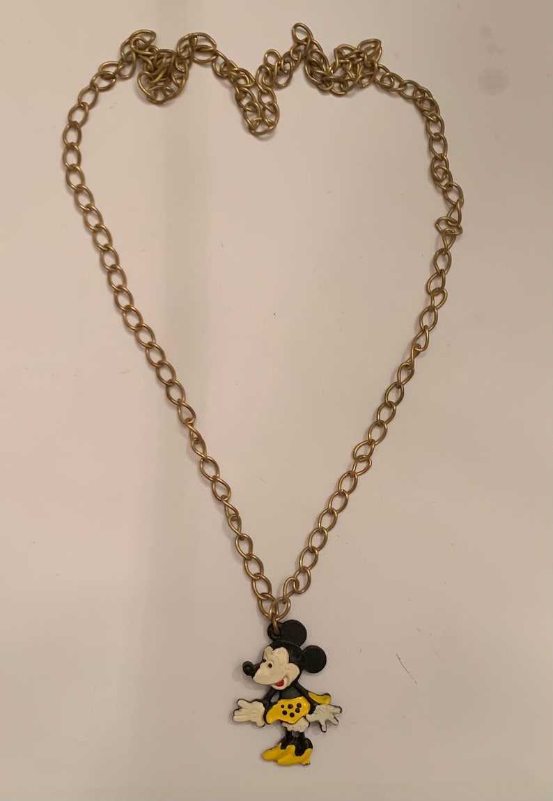Puede incluir: Un collar de cadena dorada con un colgante de Mickey Mouse de esmalte negro, blanco y amarillo.