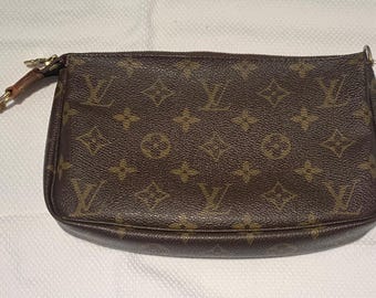 May include: A brown pouch featuring the iconic LV monogram pattern in a repeating design. The accessory includes a gold-tone zipper closure with a tan leather pull tab attached to the side, showcasing a textured finish throughout the exterior.
