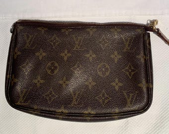 May include: A rectangular brown pouch featuring a repeating dark brown monogram pattern of stylized flowers and the letters LV. The accessory has a gold-toned metal zipper closure along the top edge with a small brown leather pull tab attached.