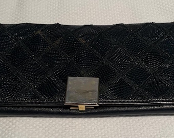 May include: A rectangular black wallet featuring a quilted diamond pattern across the front flap. The wallet is secured with a smooth, square-shaped silver-toned metal clasp centered on the lower edge of the flap.