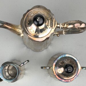 Puede incluir: Un juego de t&eacute; plateado, que incluye una tetera, azucarero y lechera. La tetera tiene un pico curvo y un pomo negro en la tapa. El juego tiene un patr&oacute;n decorativo en relieve.