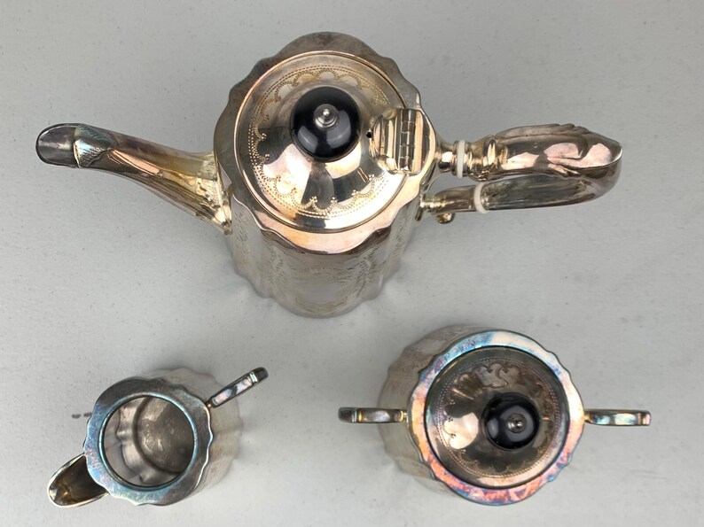 Puede incluir: Un juego de t&eacute; plateado, que incluye una tetera, azucarero y lechera. La tetera tiene un pico curvo y un pomo negro en la tapa. El juego tiene un patr&oacute;n decorativo en relieve.