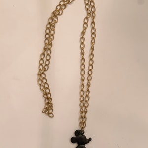 Puede incluir: Un collar de cadena dorada con una silueta negra de Minnie Mouse como colgante.