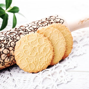 Puede incluir: Un rodillo de madera con un diseño floral y el texto "Alisa Crafts" en el mango. Cuatro galletas con un diseño floral están al lado del rodillo.