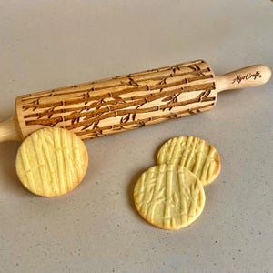 May include: A wooden rolling pin with a bamboo design and the text "Algis Crafts" on the handle. Three round cookies with a bamboo pattern are next to the rolling pin. The rolling pin is approximately 15 inches long.
