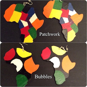 Puede incluir: Dos pares de pendientes de madera coloridos con forma del continente africano. Un par es un mosaico de rojo, amarillo, verde, azul y blanco. El otro par tiene un fondo negro con círculos rojos, amarillos, naranjas, blancos y verdes. El texto "Patchwork" y "Bubbles" está escrito debajo de cada par de pendientes.