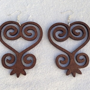 Puede incluir: Un par de pendientes de madera marrón en forma de corazón con un patrón de espiral. Los pendientes están hechos de madera y tienen ganchos de plata.