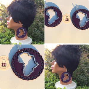 Puede incluir: Un par de pendientes grandes, redondos, de color morado con un contorno plateado. Los pendientes presentan un recorte del continente africano, que está decorado con diamantes de imitación plateados.