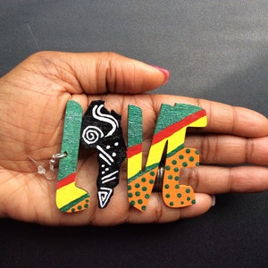 Puede incluir: Pendientes de madera con forma de la palabra "LOVE" con un esquema de colores verde, amarillo, rojo y naranja. La "L" presenta un diseño gráfico en blanco y negro.