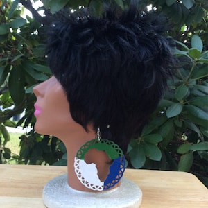 Puede incluir: Un par de pendientes de cuero verde, blanco y azul con forma del continente africano. Los pendientes tienen un diseño de encaje alrededor del borde.