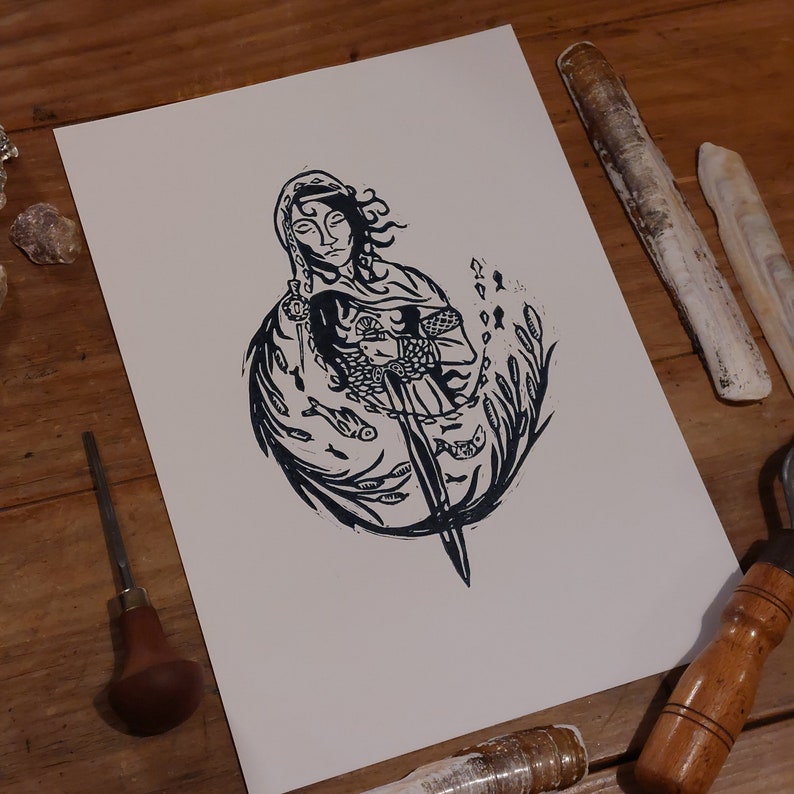 May include: Black and white linocut print of a woman holding a sword, surrounded by fish and seaweed.
