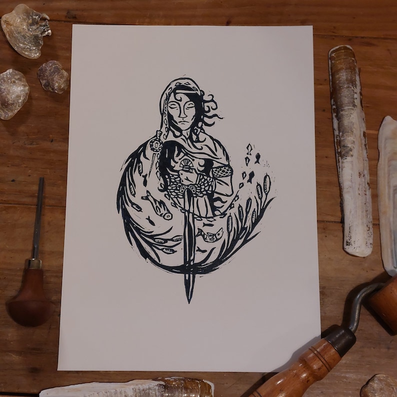 May include: Black and white linocut print of a woman holding a sword, surrounded by stylised fish and seaweed. The woman is wearing a hooded cloak and has long hair.