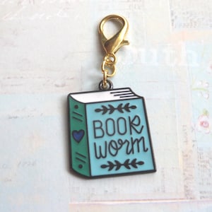 May include: A gold book charm with a blue and green enamel finish. The charm features the text "Book Worm" with a small heart in the corner.
