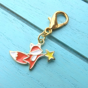 May include: A gold charm featuring a red and white fox holding a yellow star. The charm has a gold lobster clasp.
