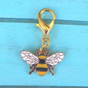 Peut inclure: Un charme en forme d'abeille dorée avec des rayures noires et jaunes et des ailes blanches. Le charme est attaché à une chaîne dorée et un fermoir à homard doré.