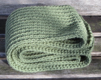 May include: A green knitted scarf folded on a wooden surface.
