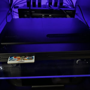 May include: Black electronic device with a card inserted, illuminated by blue light. The card displays a colorful graphic. Other electronic components are visible in the background.