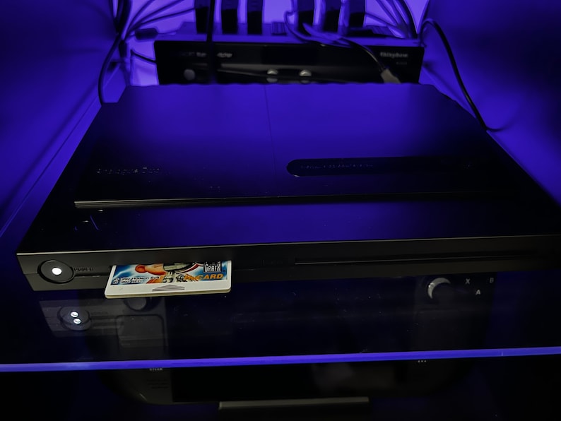 May include: Black electronic device with a card inserted, illuminated by blue light. The card displays a colorful graphic. Other electronic components are visible in the background.