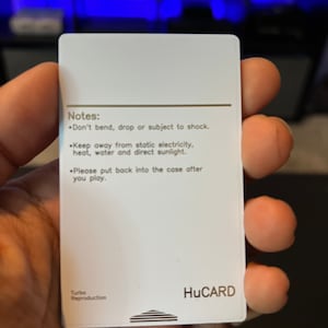 May include: A white HuCARD with printed text. The text includes "Notes: Don't bend, drop or subject to shock. Keep away from static electricity, heat, water and direct sunlight. Please put back into the case after you play."