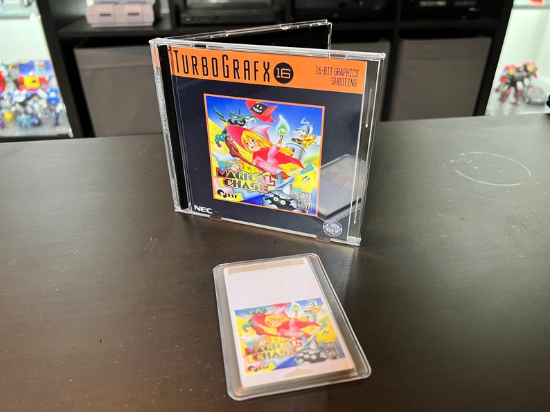 May include: A TurboGrafx-16 video game case with the game "Magic Chase" visible inside. The case is clear plastic, and the game cartridge is also visible. The game's cover art features a cartoon-style illustration with bright colors. The text "16-BIT GRAPHICS SHOOTING" is printed on the case.