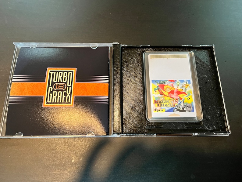 May include: A TurboGrafx-16 game cartridge and case. The case is open, revealing the game cartridge with the title "Magical Chase" and the TurboGrafx-16 logo on the case cover. The case is black with orange and white accents.