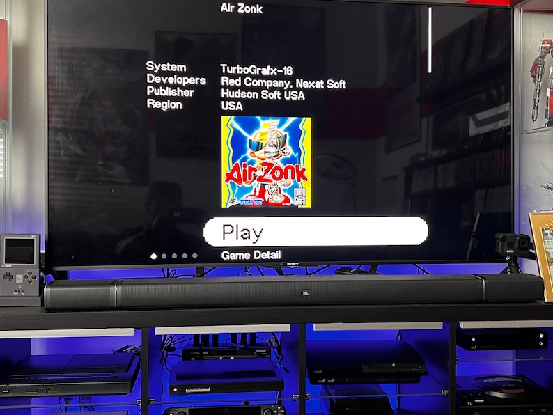 May include: A television screen displays the game "Air Zonk" for the TurboGrafx-16 system. The game's title is in red and yellow, with a cartoon character. The screen shows "Play" and "Game Detail" options. A black soundbar sits below the screen.