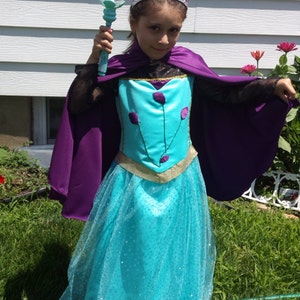 May include: A costume dress featuring a turquoise bodice with purple floral accents, a gold waistband, and a glittery turquoise skirt. The outfit includes a purple cape, a silver-toned tiara with the word PRINCESS, and a light blue wand.