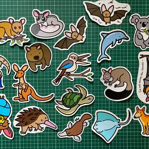 May include: A set of 15 colorful stickers featuring various Australian animals, including a koala, a kangaroo, a platypus, a echidna, a bat, a dolphin, a kookaburra, a wombat, a sugar glider, and a stingray. The stickers are printed on white paper with black outlines and are perfect for adding a touch of Australian wildlife to your belongings.