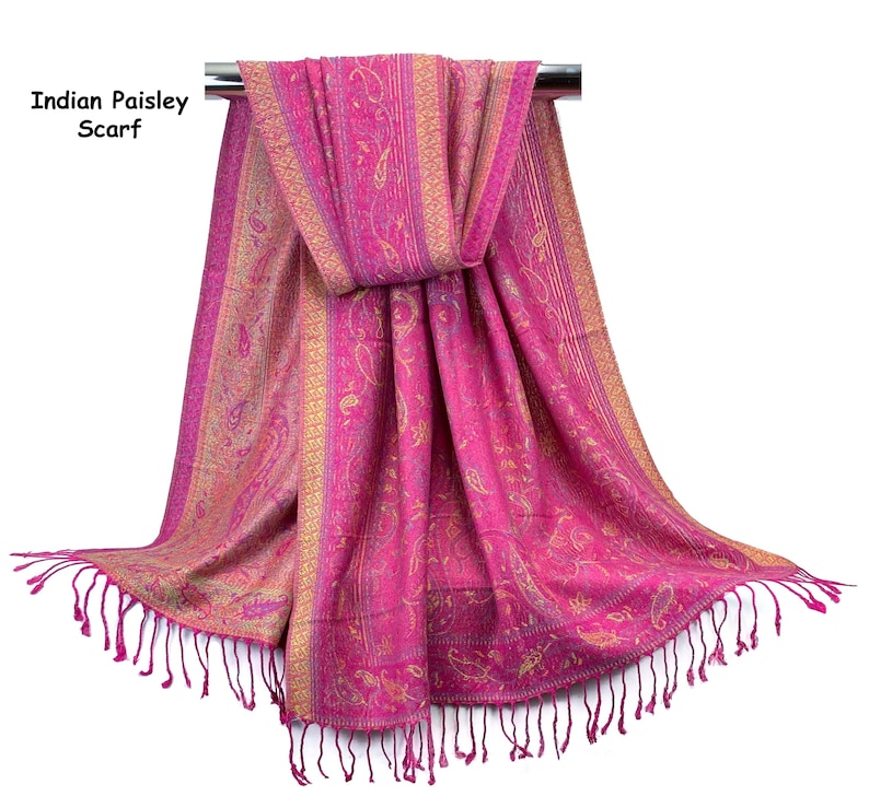 May include: A vibrant fuchsia scarf featuring an intricate gold paisley pattern throughout the fabric. The scarf includes vertical border detailing and is finished with long, matching fuchsia fringe at the bottom edges. Text reads Indian Paisley Scarf.