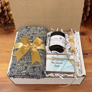 May include: A gift box filled with a blue and gold patterned scarf, a jar of hand and body moisturizer, a small bottle of lavender bath salts, and a bar of all-natural handmade soap.