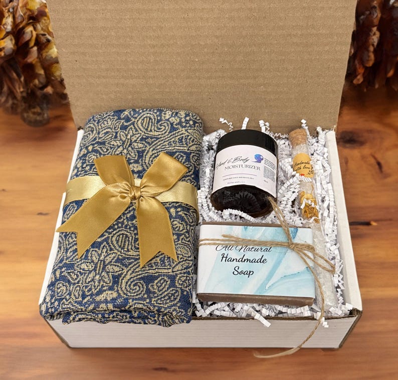 May include: A gift box filled with a blue and gold patterned scarf, a jar of hand and body moisturizer, a small bottle of lavender bath salts, and a bar of all-natural handmade soap.