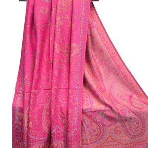 May include: A vibrant fuchsia pink shawl featuring an intricate woven paisley pattern in shades of orange, purple, and light pink. The fabric displays a dense, textured design with a wide decorative border along the edge, draped over a metal rod.