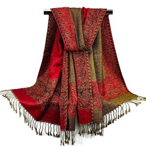 Pode incluir: Um xale vermelho e verde com padr&atilde;o paisley e franjas douradas. O xale est&aacute; dobrado ao meio e pendurado em um cabide.
