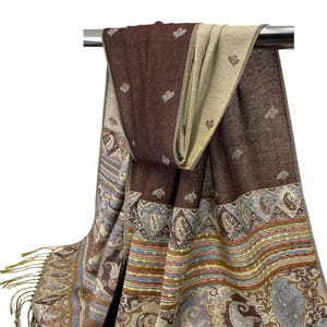 K&ouml;nnte beinhalten: Ein brauner und beiger Schal mit einem detaillierten Paisley- und Streifenmuster. Der Schal hat am Ende Fransen und ist &uuml;ber einer Metallstange drapiert. Der Schal hat ein reversibles Design mit einer einfarbigen braunen und einer beigen Seite.