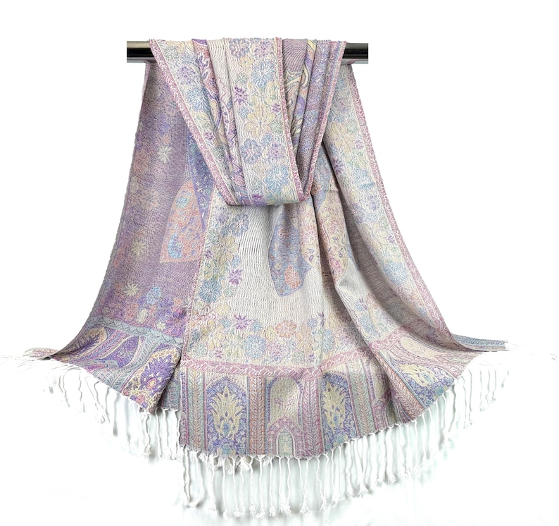 May include: A purple, pink, and cream patterned pashmina scarf with white fringe. The scarf is draped over a silver rod.