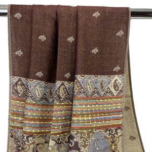 K&ouml;nnte beinhalten: Ein brauner Schal mit detailliertem Rand. Der Schal hat ein sich wiederholendes Muster aus kleinen, gestickten bienenartigen Formen. Der Rand weist Paisley- und geometrische Designs mit farbenfrohen Akzenten auf. Der Schal besteht aus einem weichen, gewebten Material.