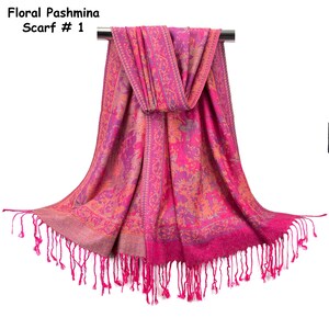 May include: A bright pink pashmina scarf featuring an intricate floral pattern in shades of orange and purple. The scarf includes a decorative border and long, thin fringe along the bottom edge. The text Floral Pashmina Scarf # 1 is visible.
