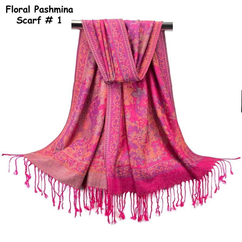 May include: A bright pink pashmina scarf featuring an intricate floral pattern in shades of orange and purple. The scarf includes a decorative border and long, thin fringe along the bottom edge. The text Floral Pashmina Scarf # 1 is visible.