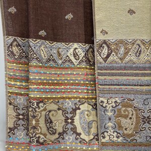 K&ouml;nnte beinhalten: Textilpaneele in Braun- und Beiget&ouml;nen mit aufwendigen Mustern. Die Paneele weisen Paisley- und geometrische Designs mit farbenfrohen, gestickten Streifen auf. Die oberen Abschnitte haben ein sich wiederholendes Blattmuster.