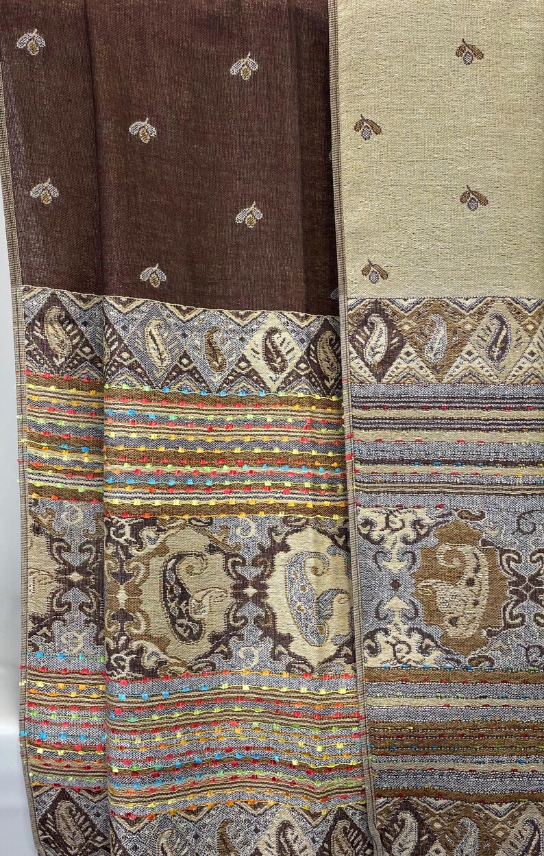 K&ouml;nnte beinhalten: Textilpaneele in Braun- und Beiget&ouml;nen mit aufwendigen Mustern. Die Paneele weisen Paisley- und geometrische Designs mit farbenfrohen, gestickten Streifen auf. Die oberen Abschnitte haben ein sich wiederholendes Blattmuster.