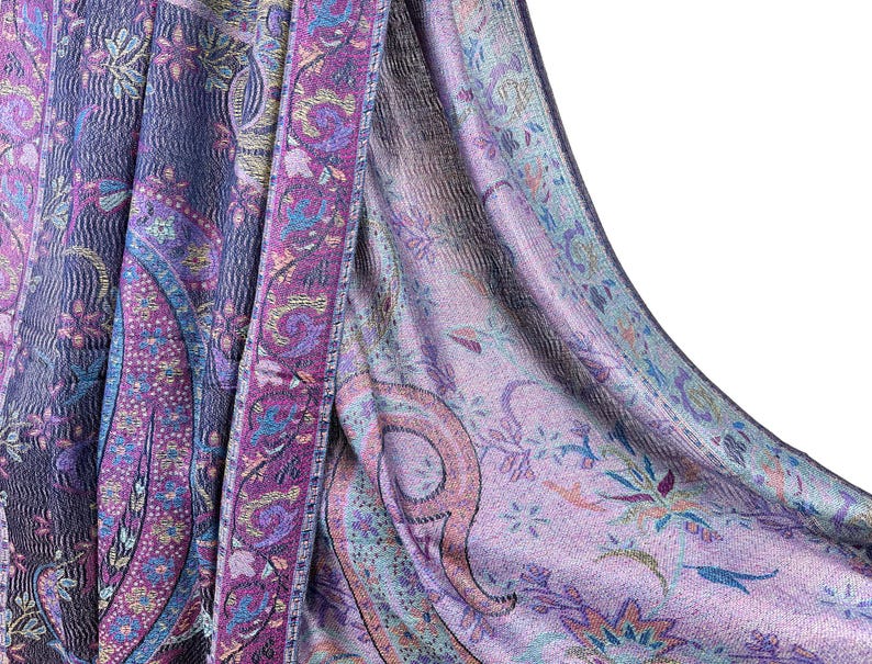 May include: A purple and blue paisley patterned shawl with a fringed edge. The shawl is made of a soft, lightweight fabric and is perfect for adding a touch of elegance to any outfit.