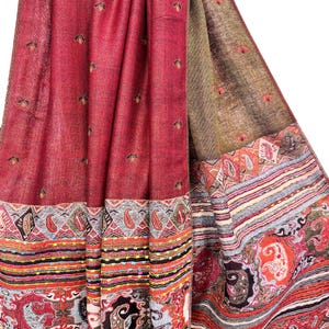 K&ouml;nnte beinhalten: Ein drapiertes Textil mit komplexem Muster in Rot-, Braun- und Oranget&ouml;nen. Der Stoff hat einen detaillierten Rand mit Paisley- und geometrischen Designs. Kleine, dunkle Blumenmotive sind &uuml;ber das Hauptfeld in Rot verstreut.