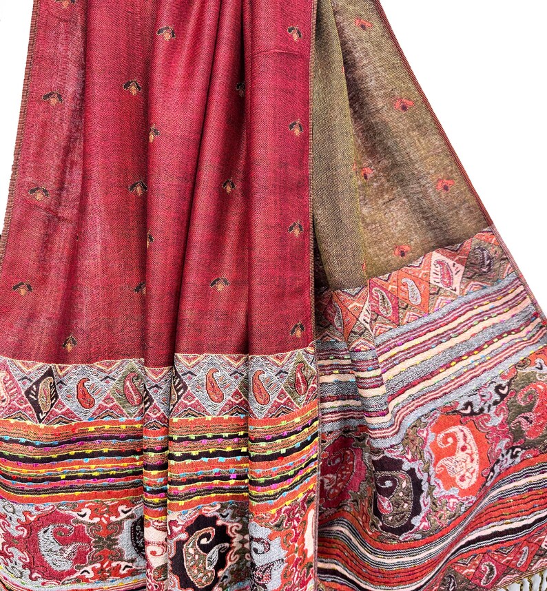 K&ouml;nnte beinhalten: Ein drapiertes Textil mit komplexem Muster in Rot-, Braun- und Oranget&ouml;nen. Der Stoff hat einen detaillierten Rand mit Paisley- und geometrischen Designs. Kleine, dunkle Blumenmotive sind &uuml;ber das Hauptfeld in Rot verstreut.